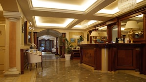 Um hall amplo com piso de mármore, balcão de recepção e um espelho grande.