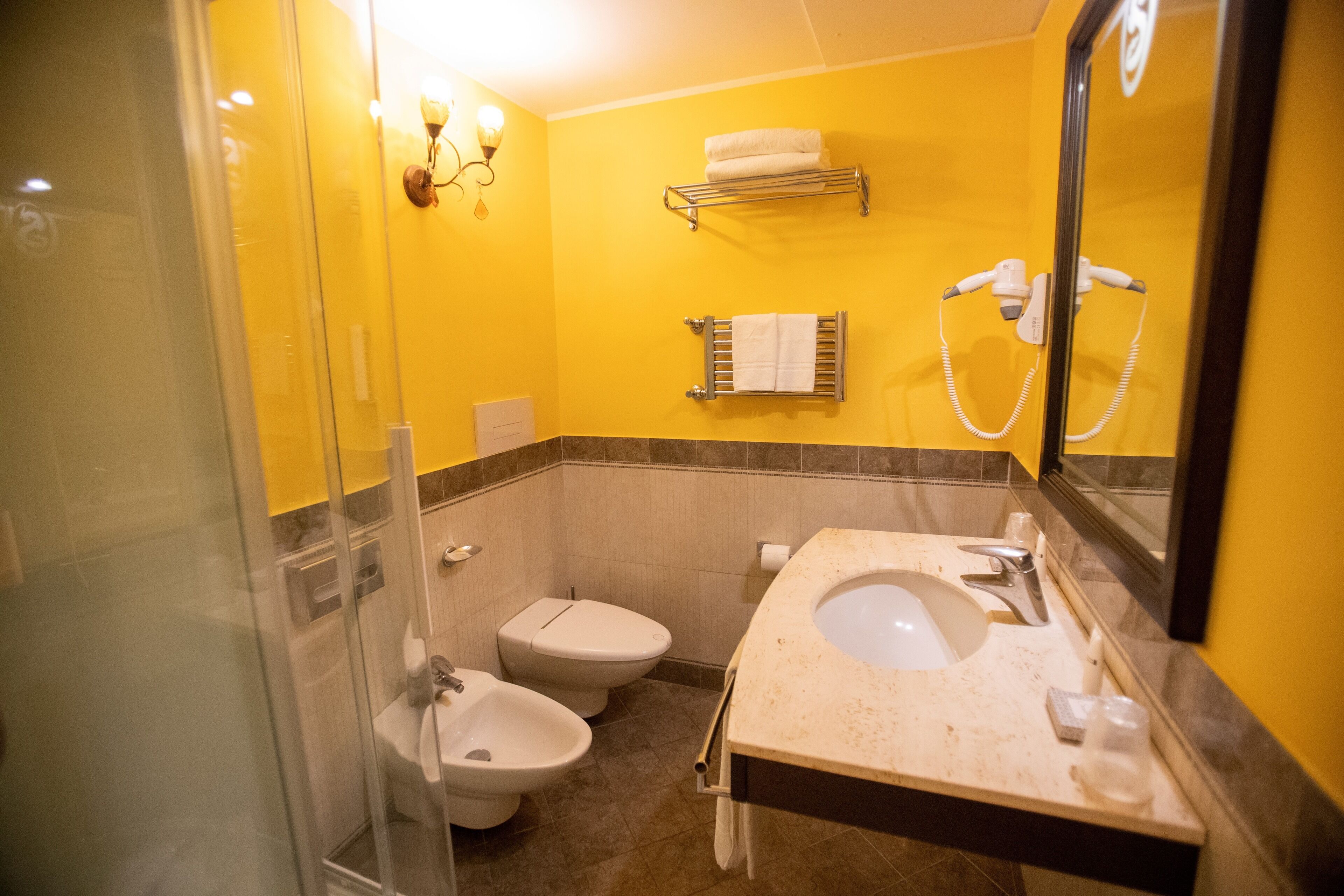 Un baño con cabina de ducha de vidrio, inodoro blanco, bidé, lavabo con espejo y toallero.