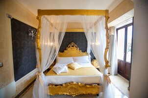 Una cama con dosel y cuatro columnas con estructura dorada, ropa de cama blanca y pared con diseño oscuro.