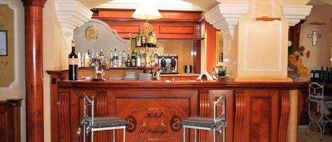 A bar area with two bar stools, a minibar, and a variety of bottles and glasses.
