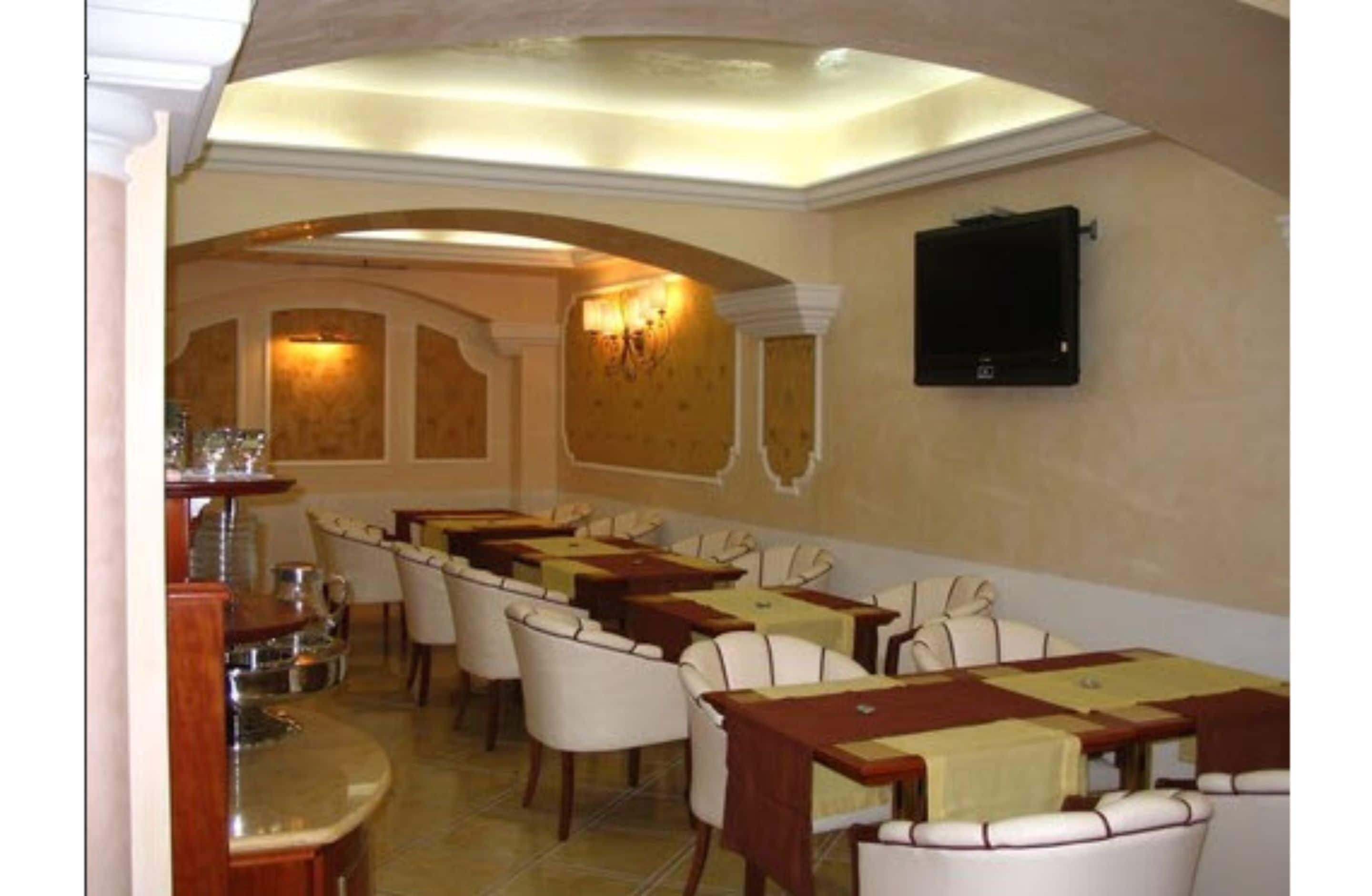 A dining area with tables and chairs, a chandelier, and a television on the wall.