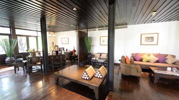 A spacious room with a wooden floor, a sofa with colorful cushions, a coffee table, and a dining table.