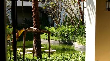 Una habitación con dos sillas de madera orientadas hacia un pequeño jardín que tiene una palmera y un estanque.