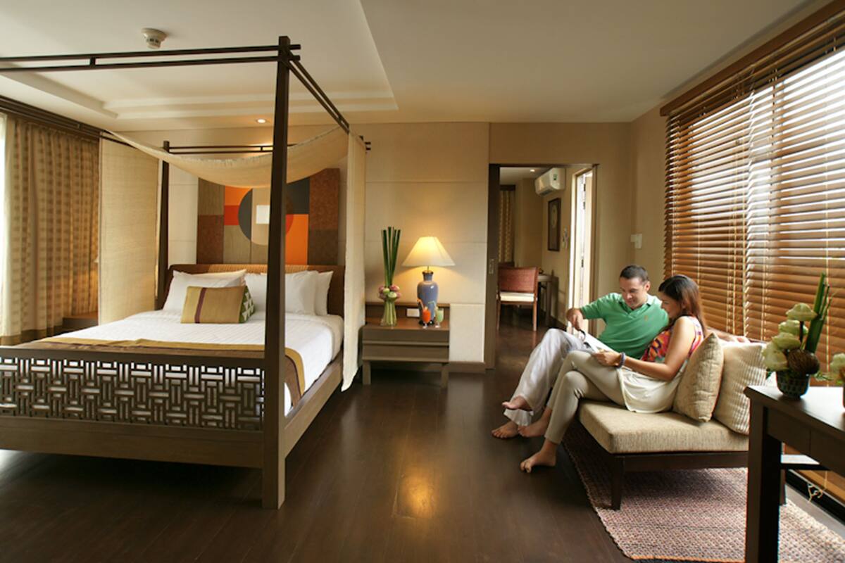 A four-poster bed with a wooden frame, a sofa, a small table, and a lamp.