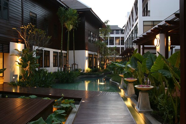 Pátio moderno de hotel com deck de madeira, uma piscina pequena e plantas tropicais exuberantes.
