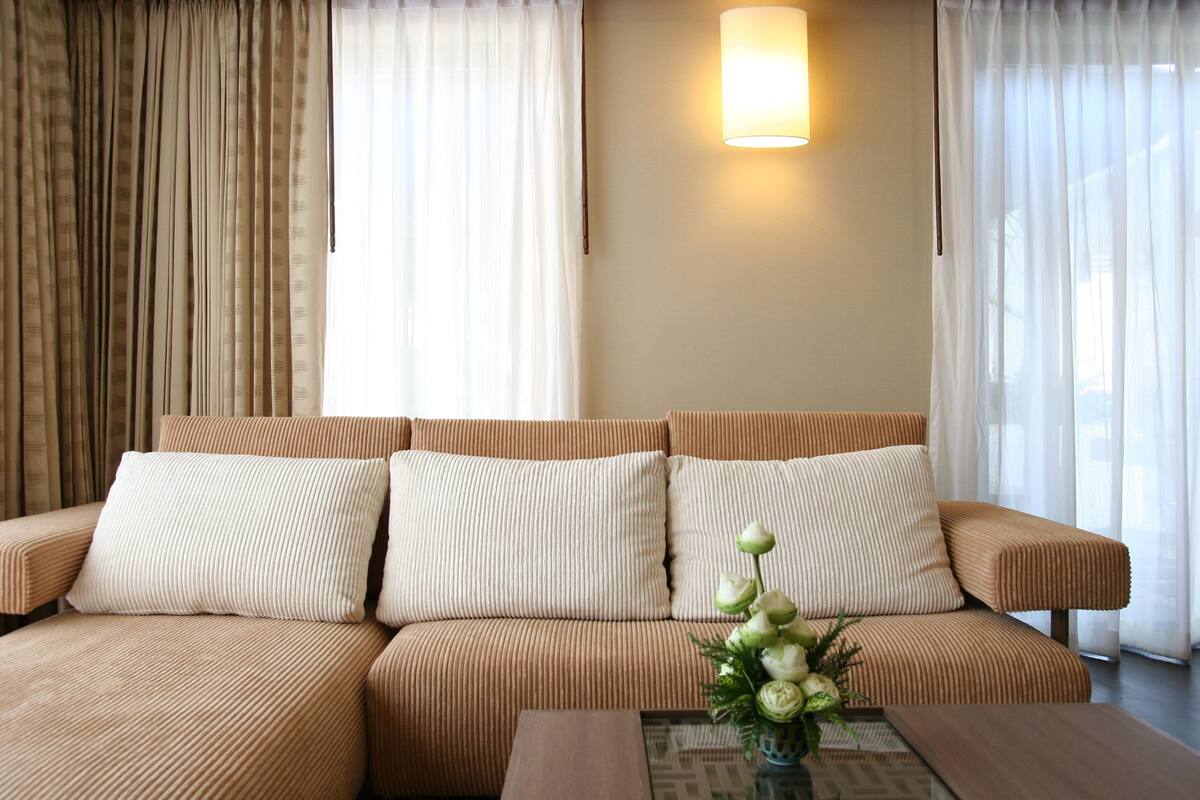 A modern living room with a brown sofa, white cushions, and a small table with a vase of flowers.