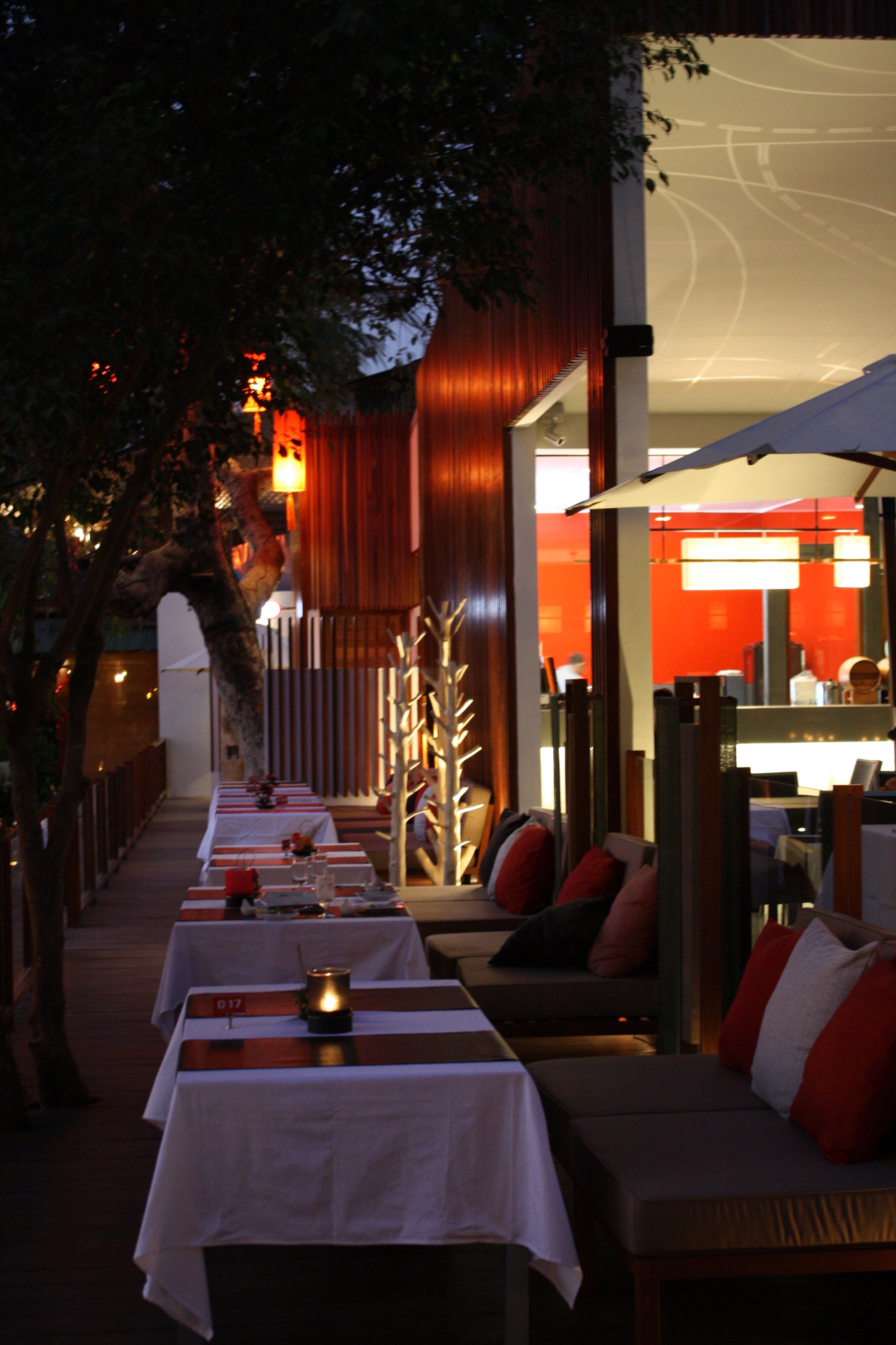 A restaurant with outdoor seating, white tablecloths, and candle centerpieces.