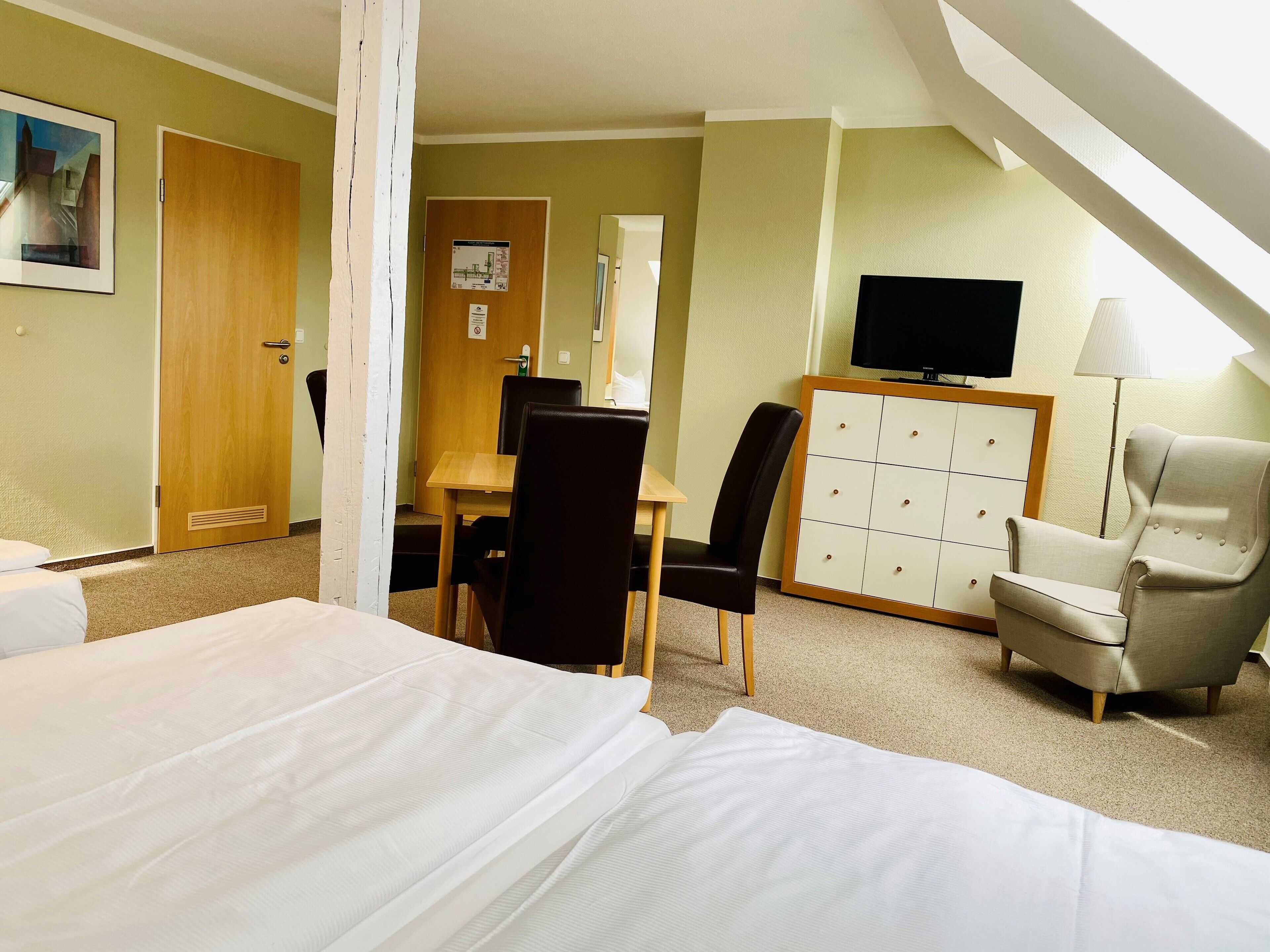 A hotel room with a bed, a desk, a chair, a TV, and a lamp.
