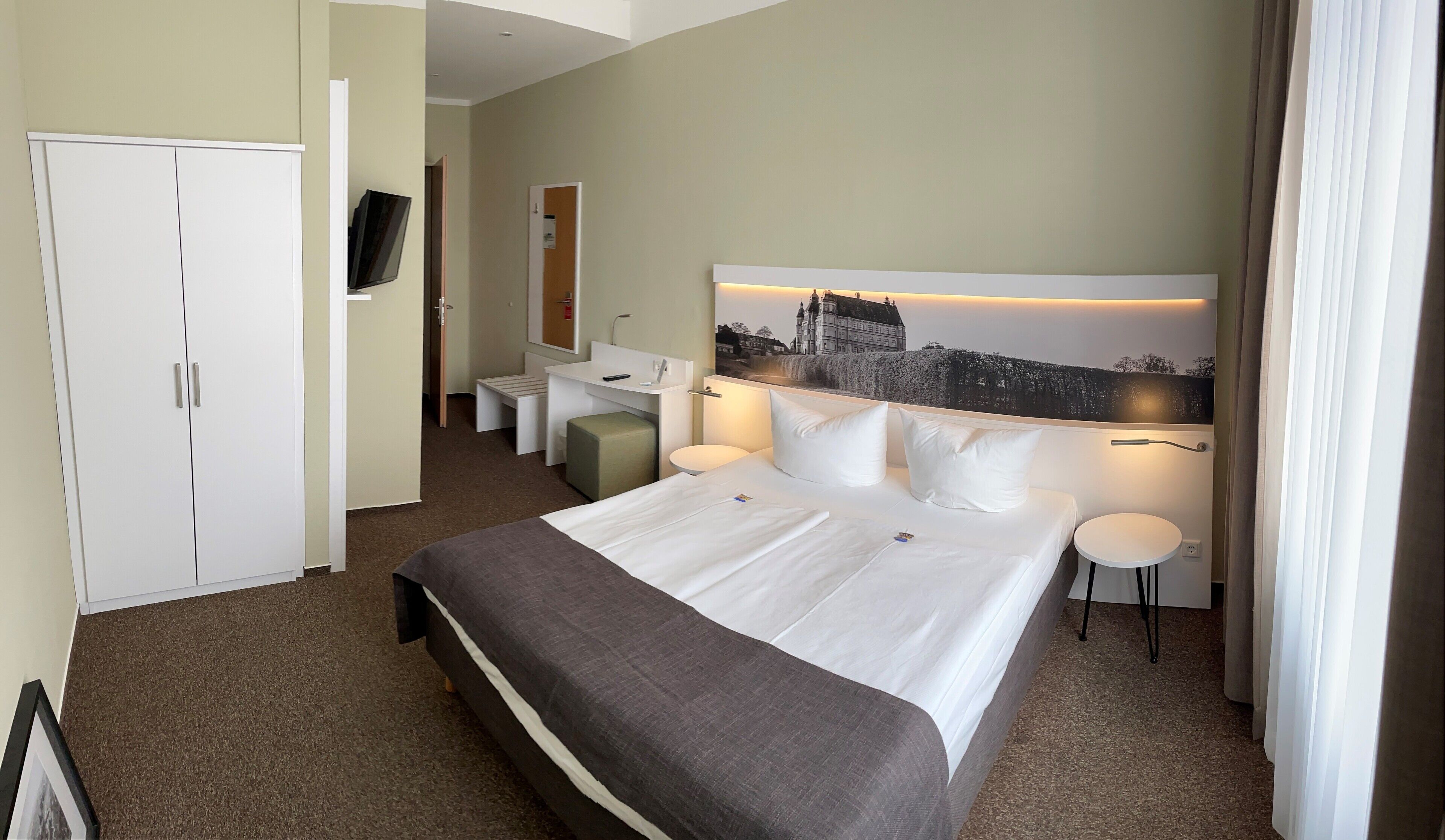 Una habitación de hotel con una cama grande, un escritorio, una silla, un televisor y un cuadro en la pared.
