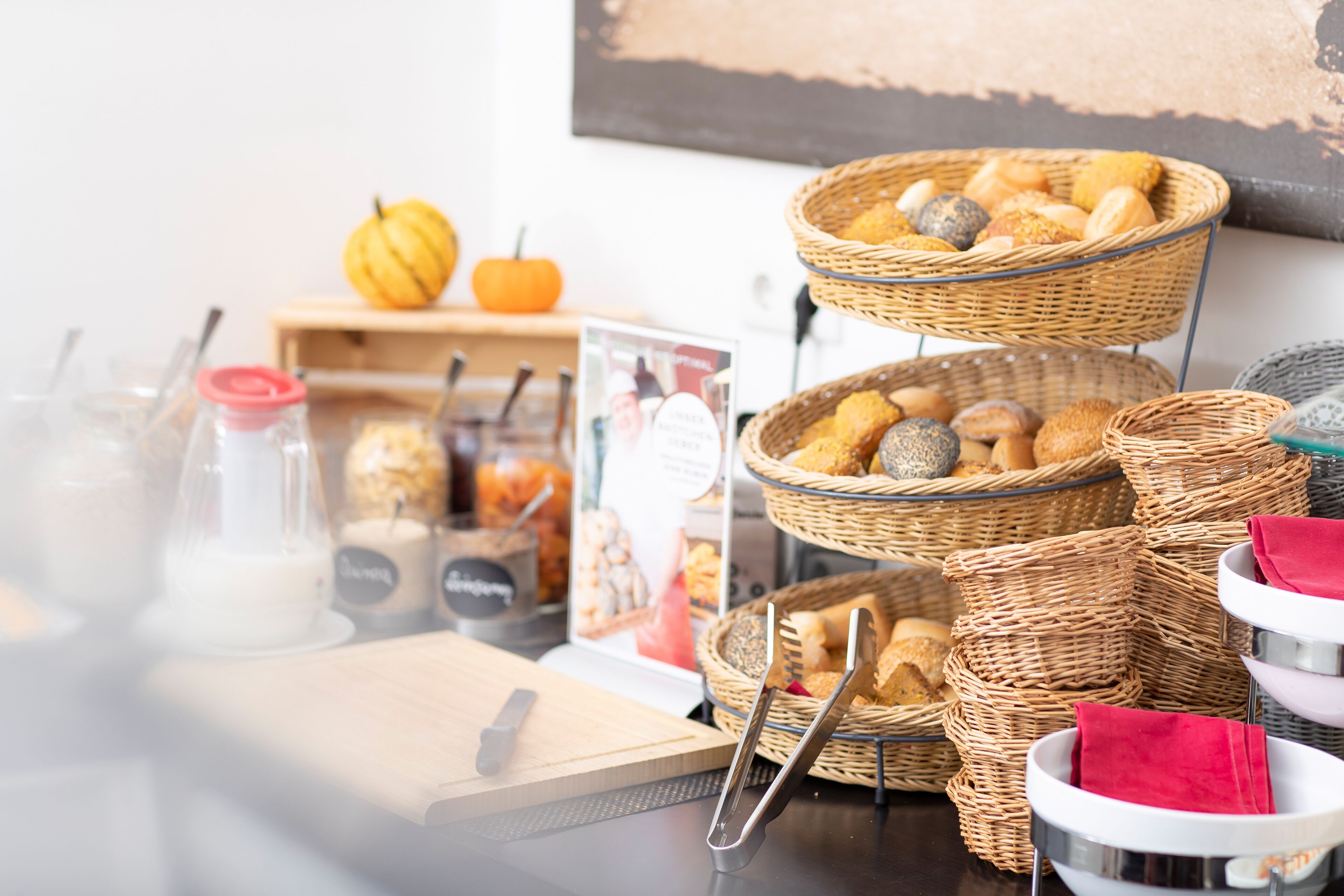 Un buffet de petit-déjeuner avec des paniers en osier remplis de viennoiseries et de pain, une planche à découper et un panneau indicateur.
