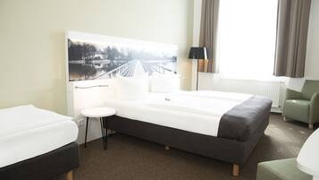 Een hotelkamer met een groot bed, een klein rond tafeltje, een stoel en een schilderij van een brug over water aan de muur.