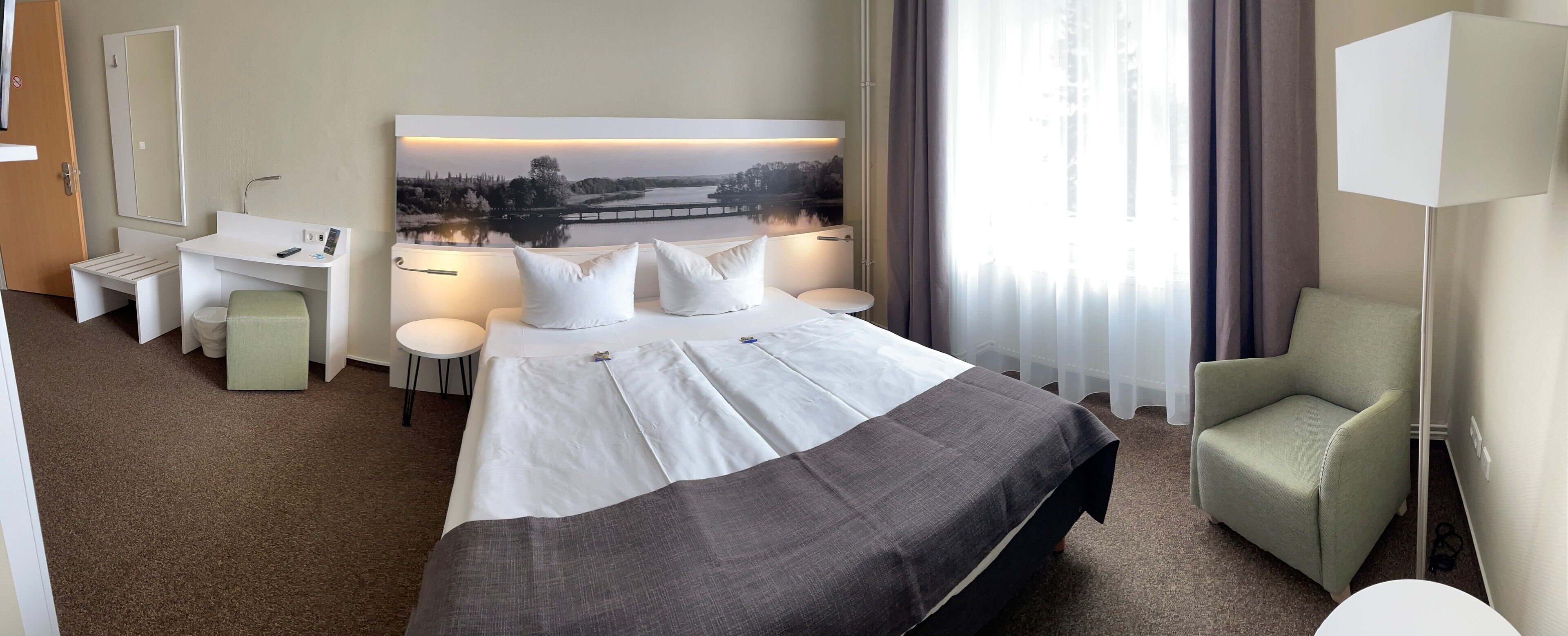 Ein Hotelzimmer mit Bett, Schreibtisch, Stuhl und einem großen Fenster mit Landschaftsblick.