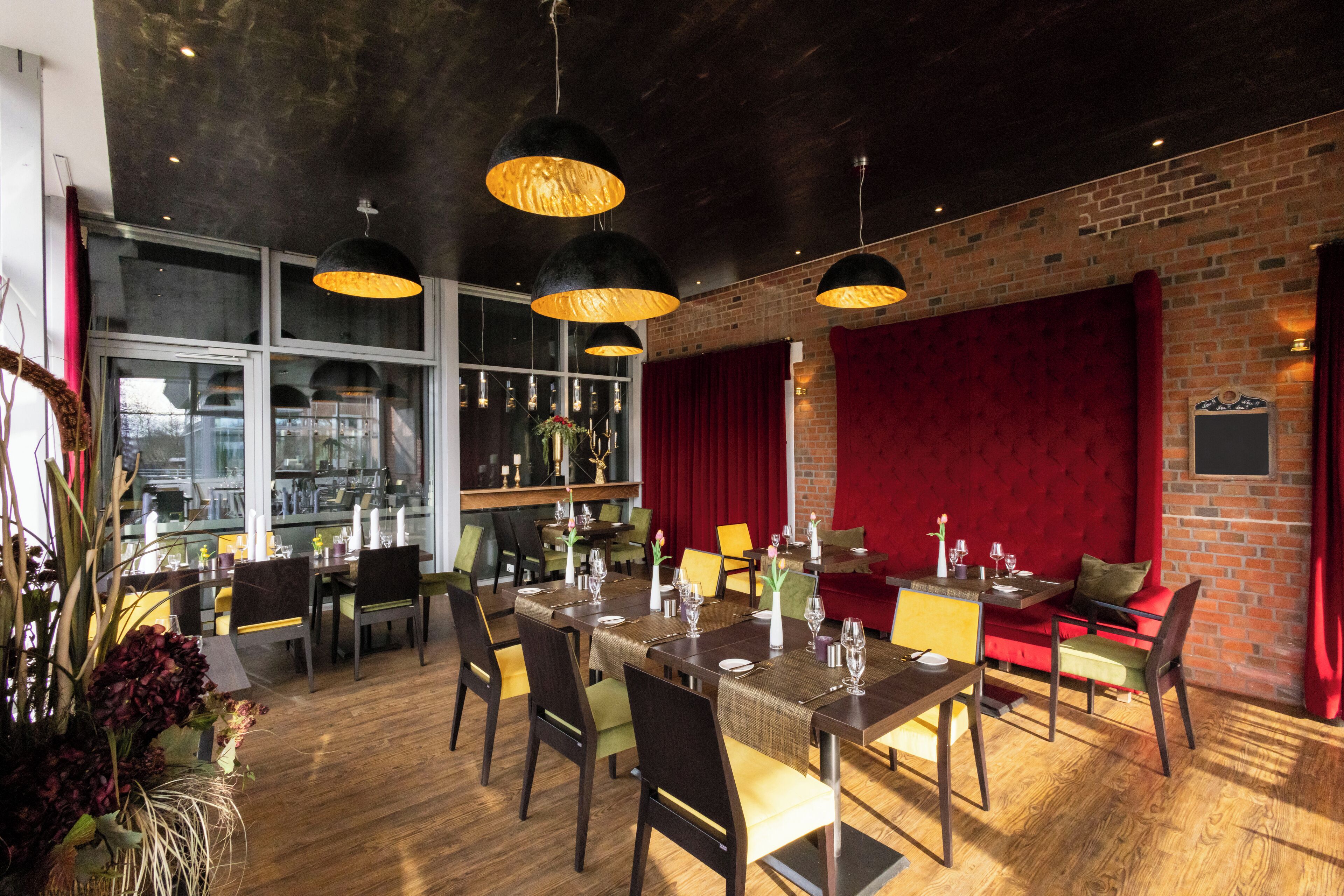 Un restaurante con pared de ladrillo, cortinas rojas y mesas y sillas de madera.
