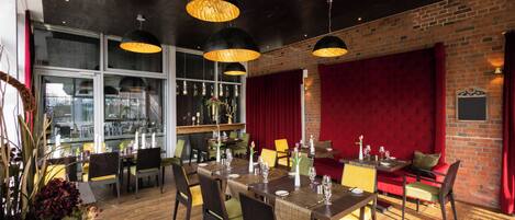 Un restaurante con pared de ladrillo, cortinas rojas y mesas y sillas de madera.