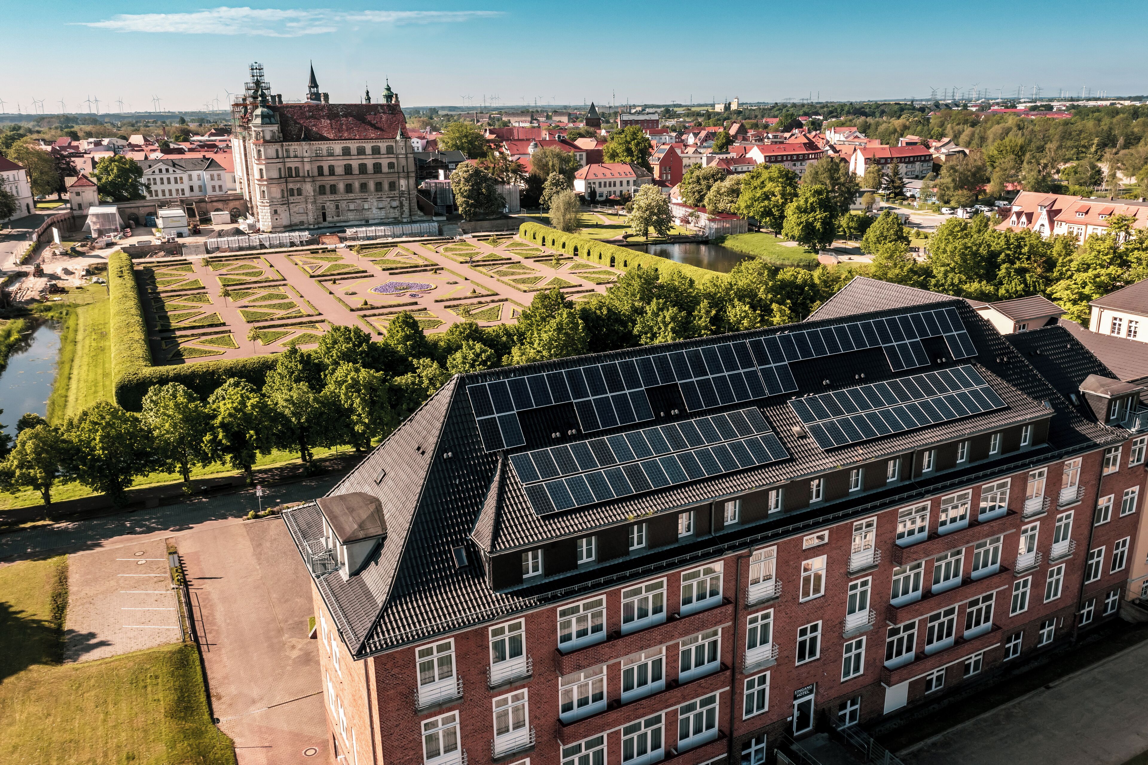 Ein Gebäude mit Solaranlage auf dem Dach, ein Innenhof mit geometrischen Mustern und ein historisches Gebäude im Hintergrund.