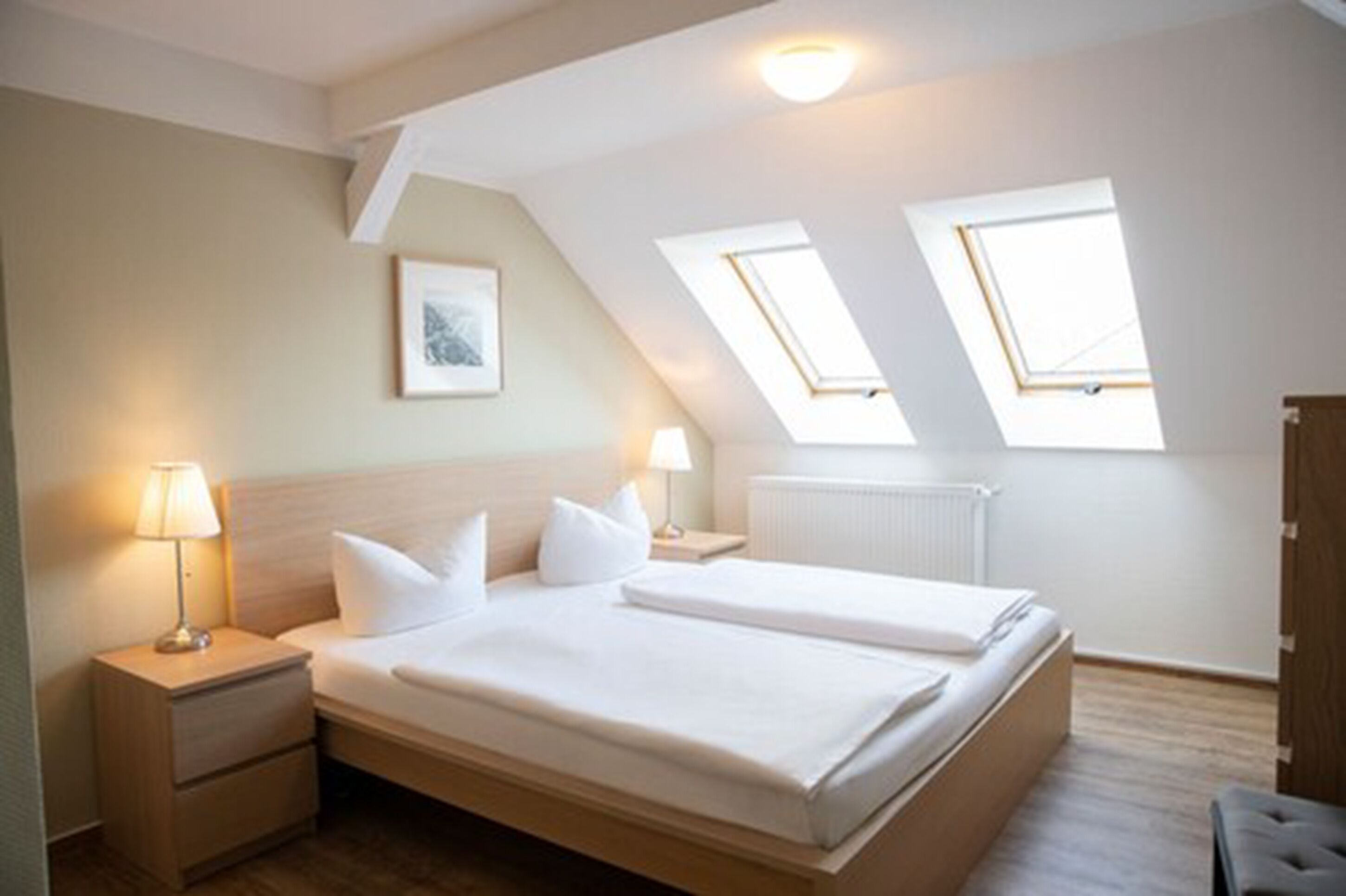Une chambre avec deux lits, une table de chevet, une lampe et un tableau encadré au mur.