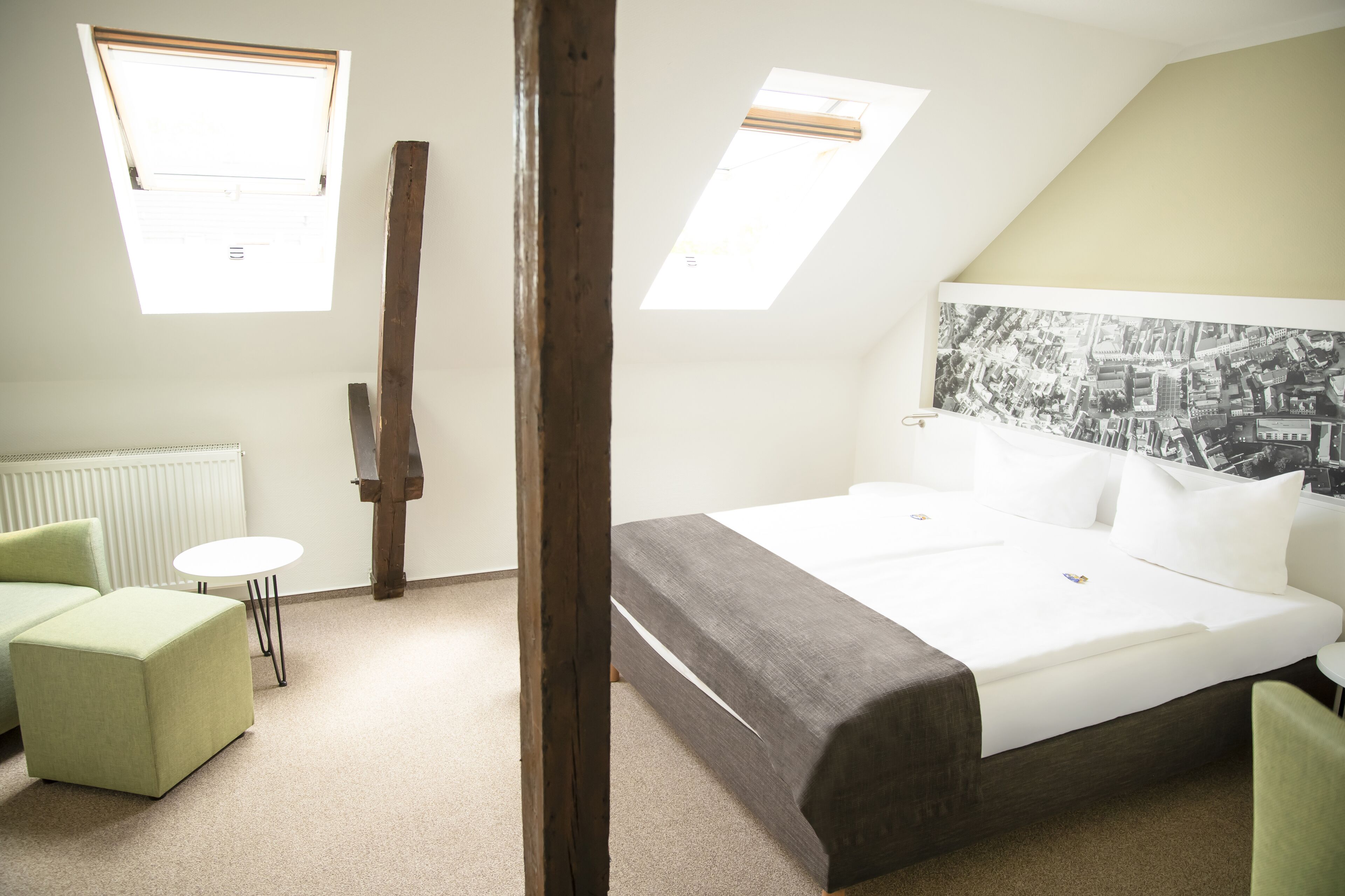A hotel room with a large bed, a green sofa, a small table, and two skylights.