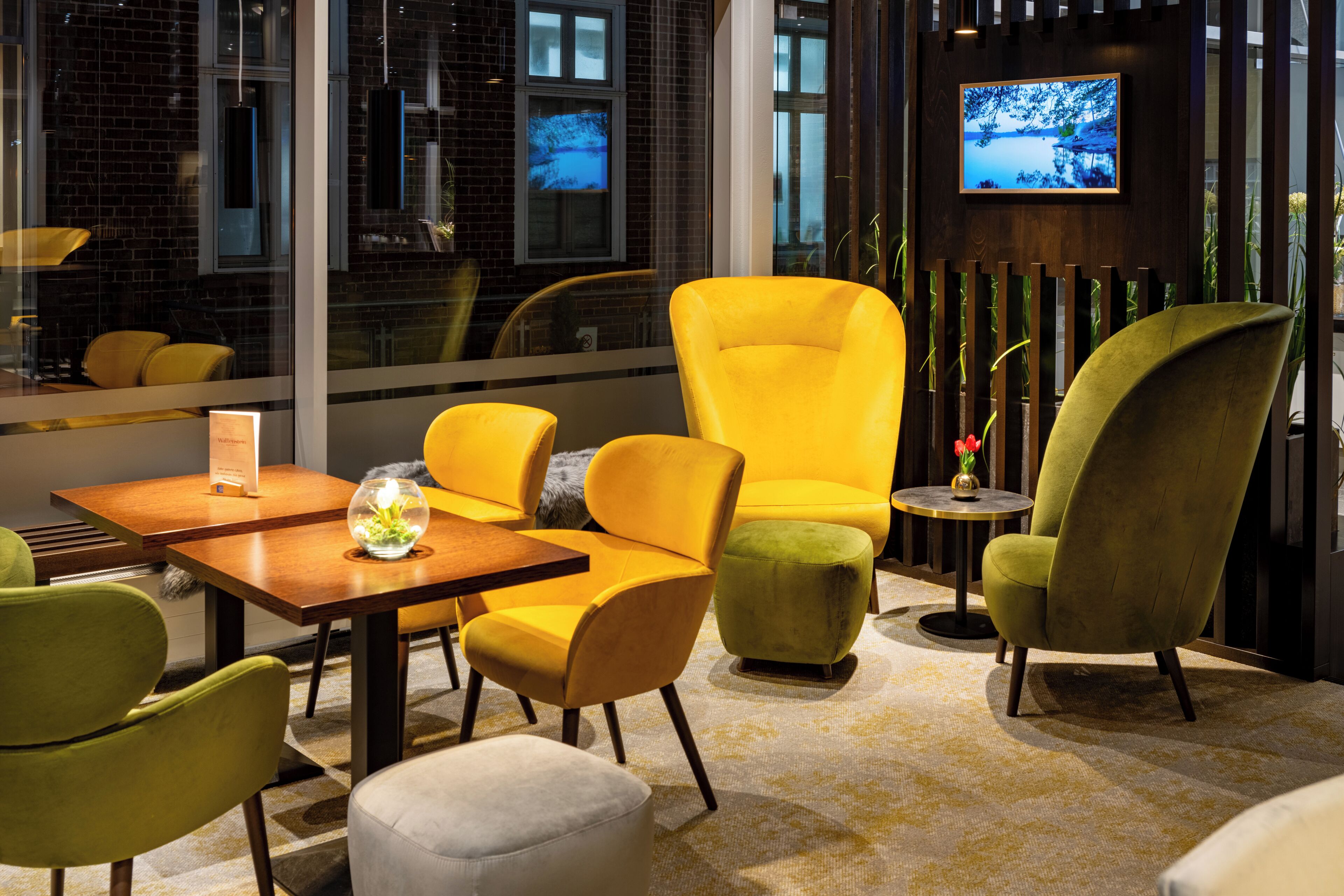 A modern interior with yellow and green chairs, a wooden table, and a TV on the wall.