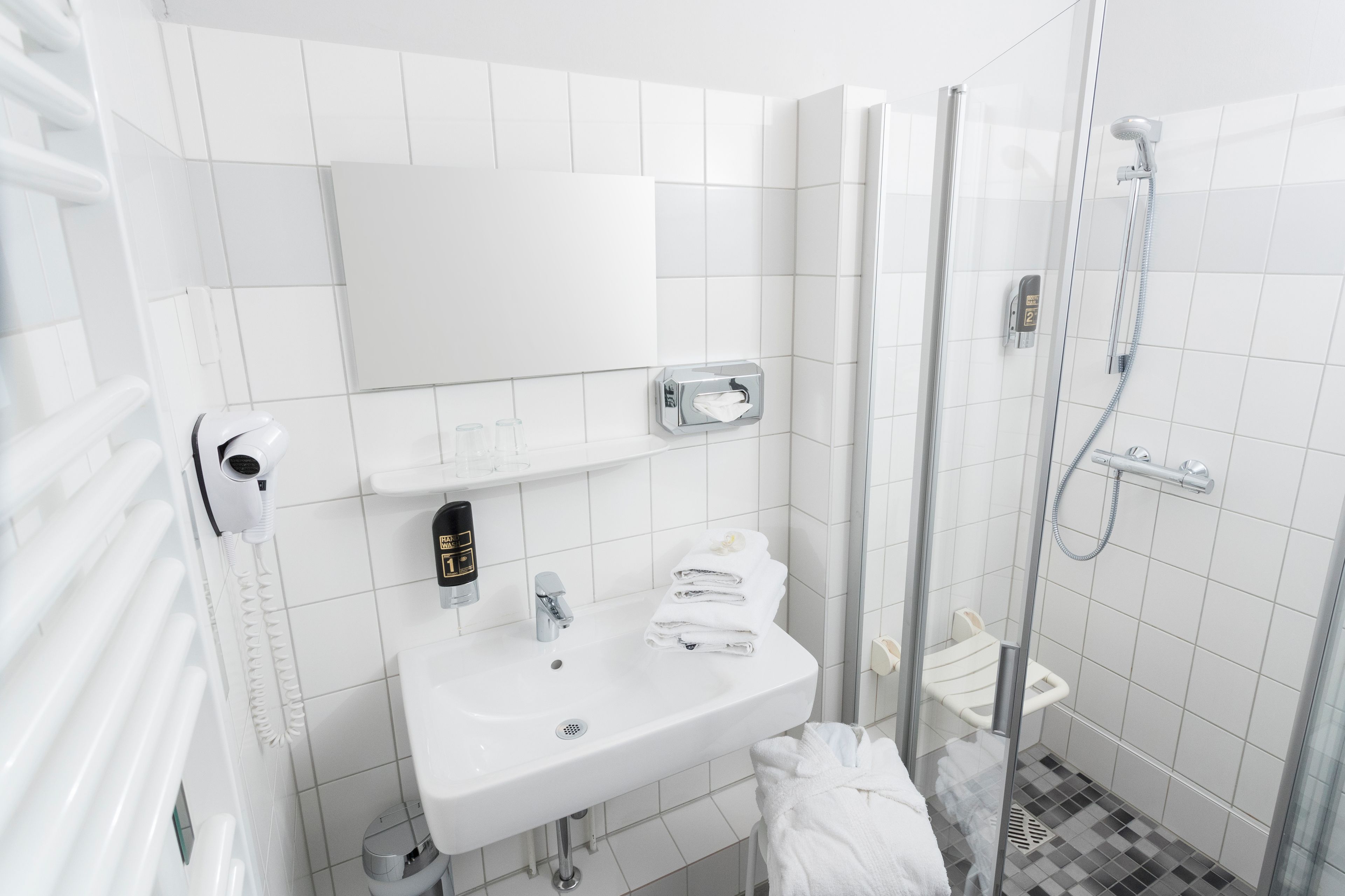 A modern bathroom with a white sink, a mirror, a towel rack, and a shower area.