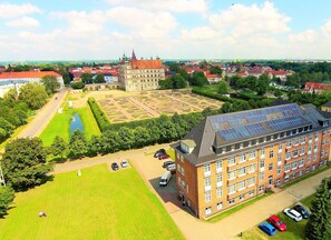 Un edificio grande con techo de paneles solares, rodeado por un césped verde y un estacionamiento con varios coches.