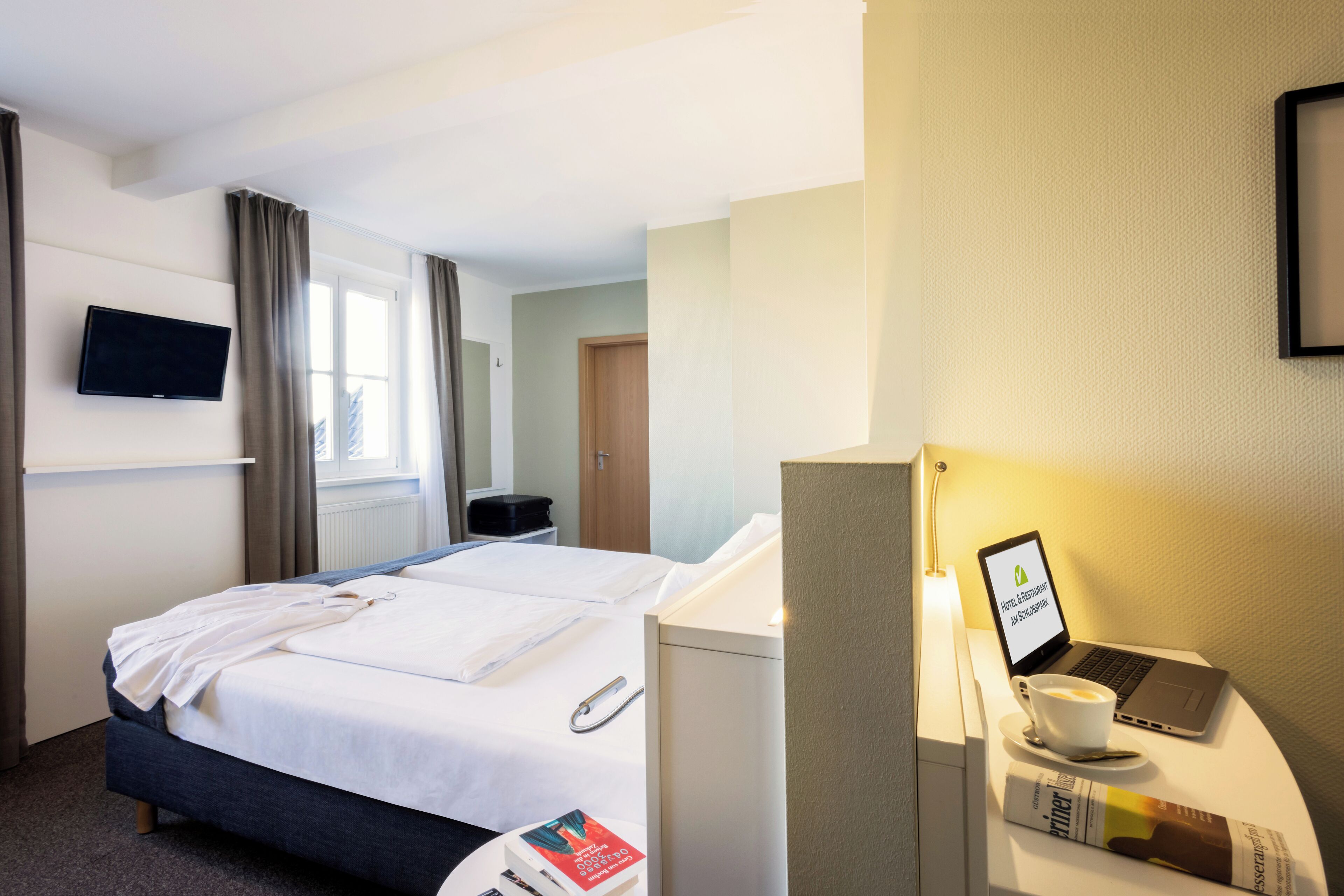 Habitación de hotel con una cama, un escritorio con una computadora portátil, una taza de café y un libro.