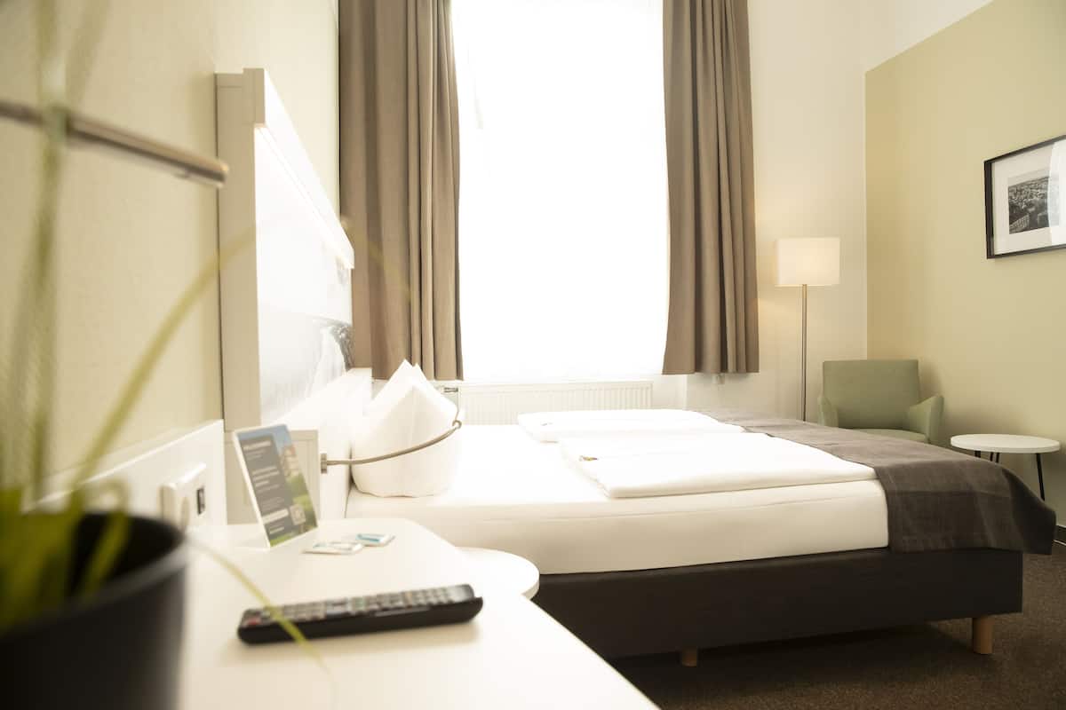 Una habitación de hotel con una cama, un escritorio con control remoto, una lámpara y una silla.