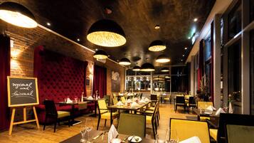 Un restaurant avec un mur en briques, des banquettes en velours rouge et plusieurs tables à manger avec des chaises jaunes.