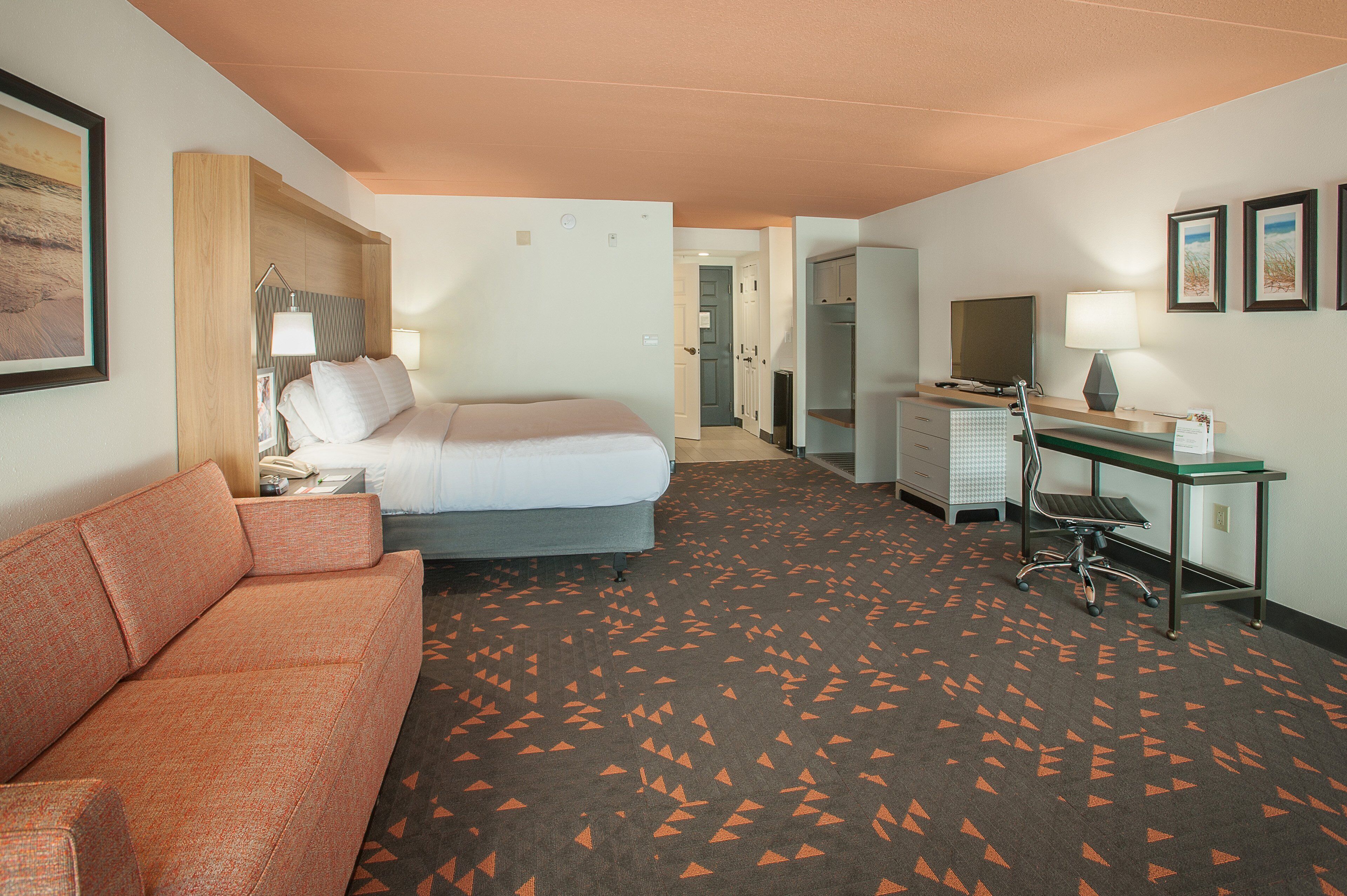 A hotel room with a bed, a sofa, a desk, and a TV.