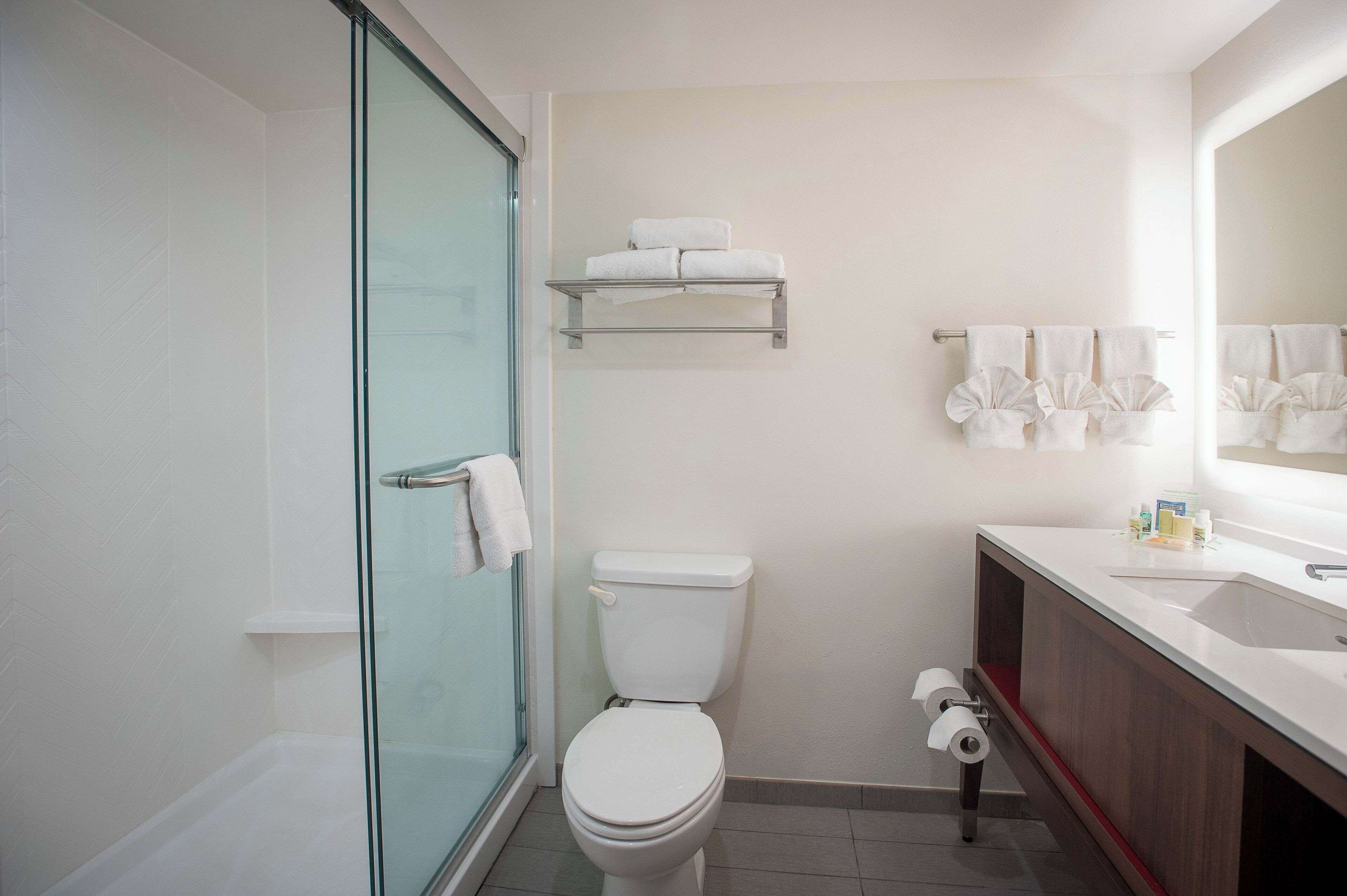 Une salle de bain avec une douche à parois de verre, des toilettes, un lavabo avec un miroir et un porte-serviettes.