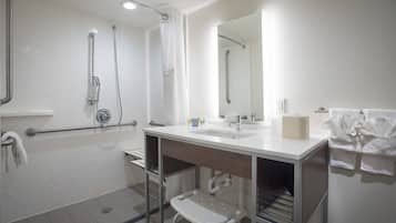 A modern bathroom with a shower, a sink, a mirror, and a step stool.