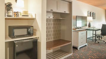 A compact hotel room with a kitchenette, a television, a desk, and a chair.
