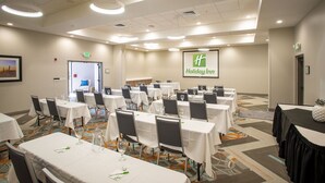 Un salón de conferencias con varias mesas y sillas, una pantalla de proyección que muestra 'Holiday Inn' y una puerta de salida.
