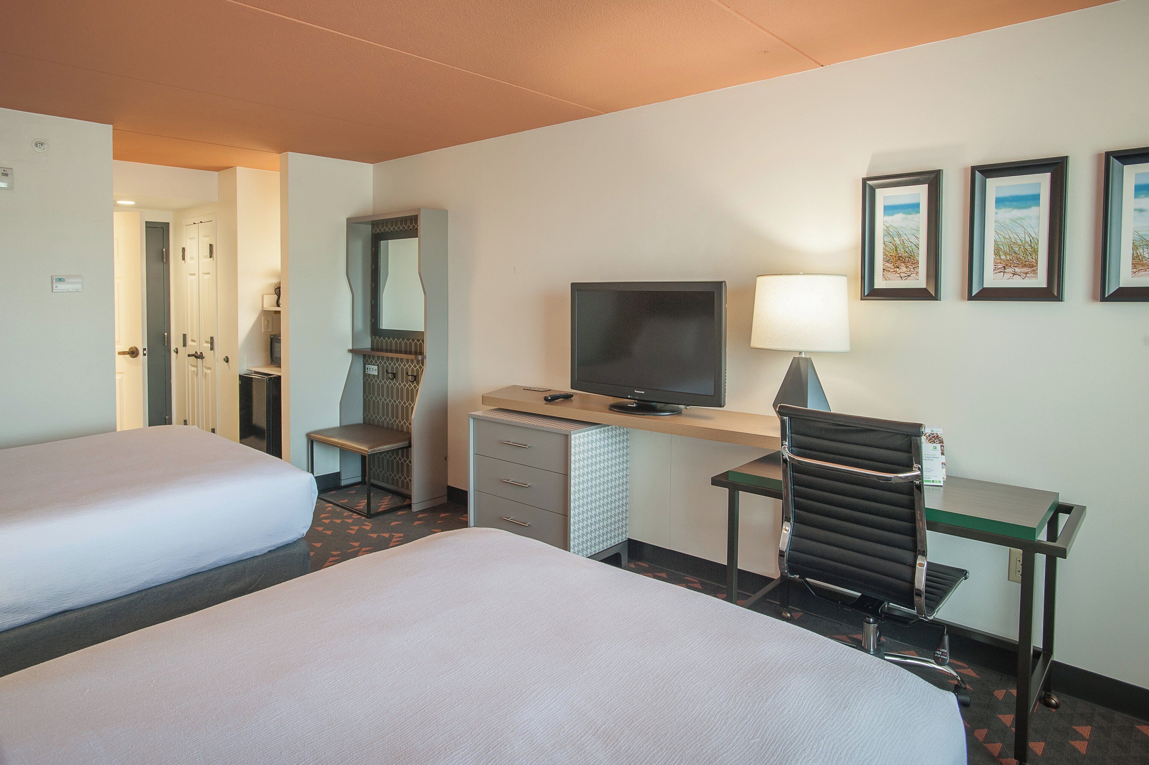 A hotel room with two beds, a desk with a television, a chair, and a desk lamp.