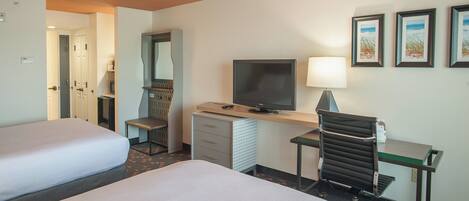 A hotel room with two beds, a desk with a television, a chair, and a desk lamp.