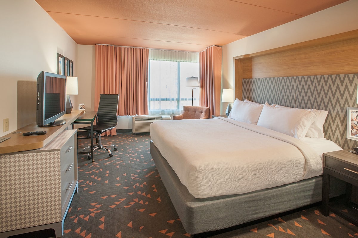 Habitación de hotel con una cama grande, un escritorio con computadora, una silla y un televisor.