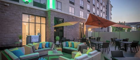 An outdoor seating area with wicker furniture and umbrellas, a brick building in the background, and a sign for the Holiday Inn.