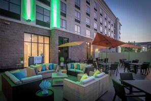 An outdoor seating area with wicker furniture and umbrellas, a brick building in the background, and a sign for the Holiday Inn. - Holiday Inn Pensacola - University Area by IHG (Pensacola)