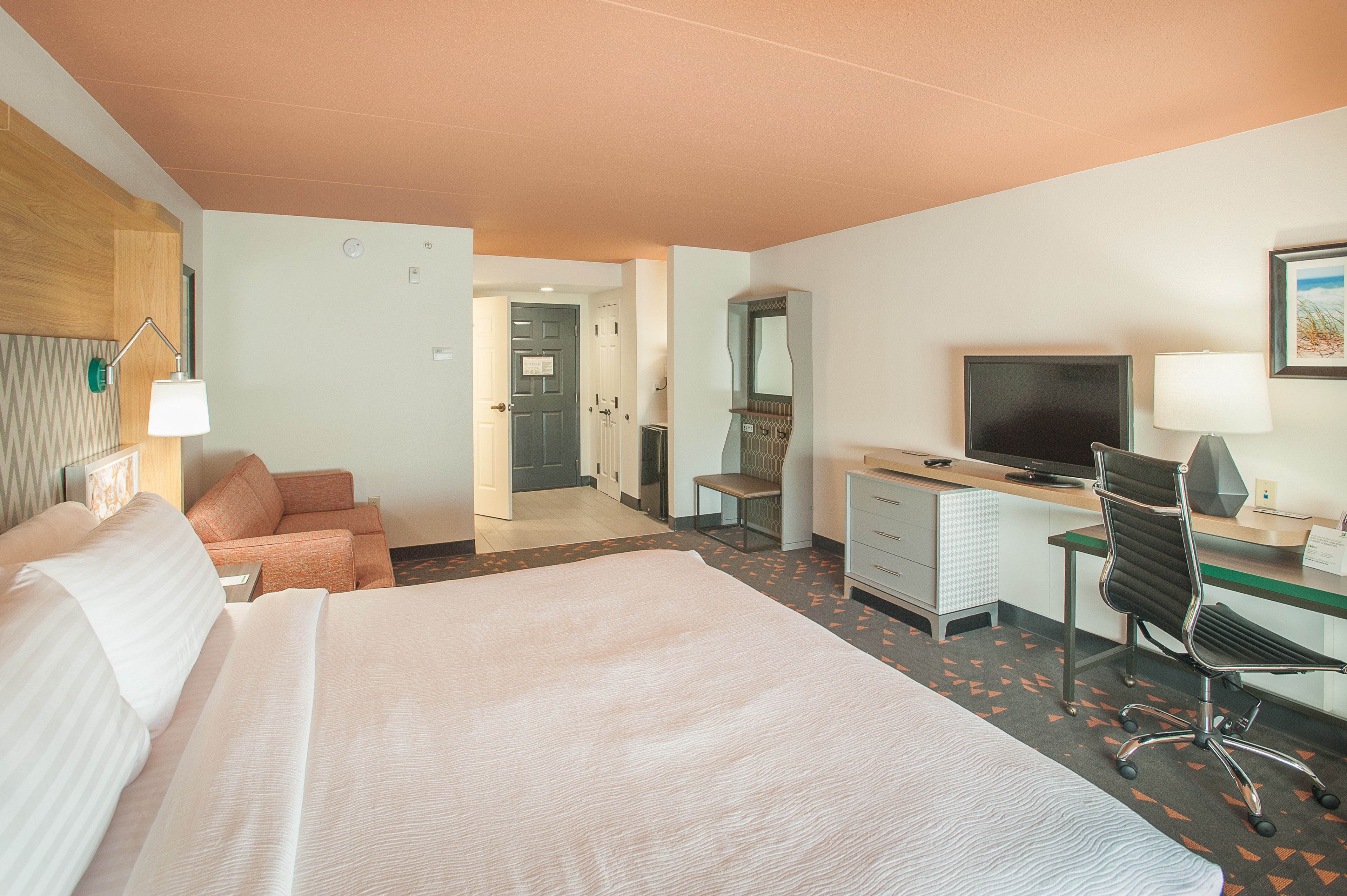 A hotel room with a large bed, a desk with a computer, a chair, and a TV.