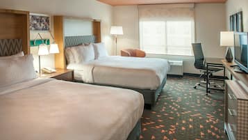 A hotel room with two beds, a desk with a TV, a chair, and a window with a view.