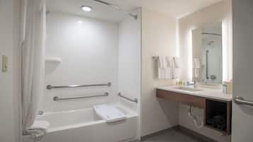 A modern bathroom with a walk-in shower, grab bars, a bathtub, a sink, and a vanity mirror.