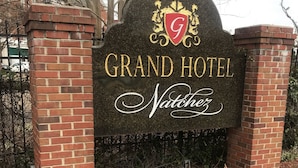 Señal del Grand Hotel Natchitoches, con un arco de ladrillo y un jardín con flores coloridas.