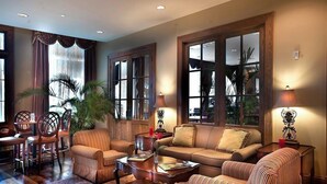 Un salón acogedor con sofá, sillones, una mesa de centro y una zona de comedor con sillas y una mesa. Amplias ventanas con cortinas dejan entrar luz natural y ofrecen vistas.