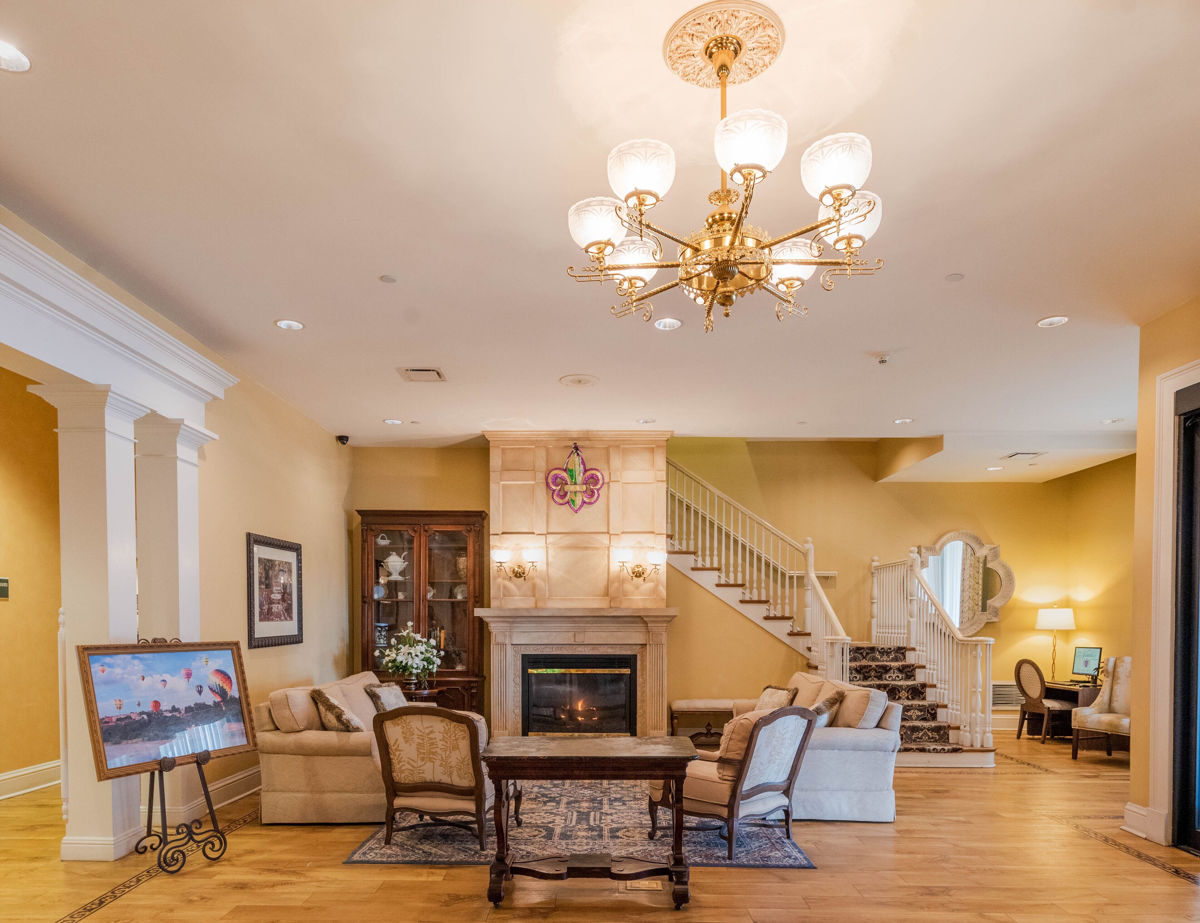 A spacious living room with a fireplace, a chandelier, and a staircase leading to an upper floor.