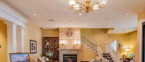 A spacious living room with a fireplace, a chandelier, and a staircase leading to an upper floor.