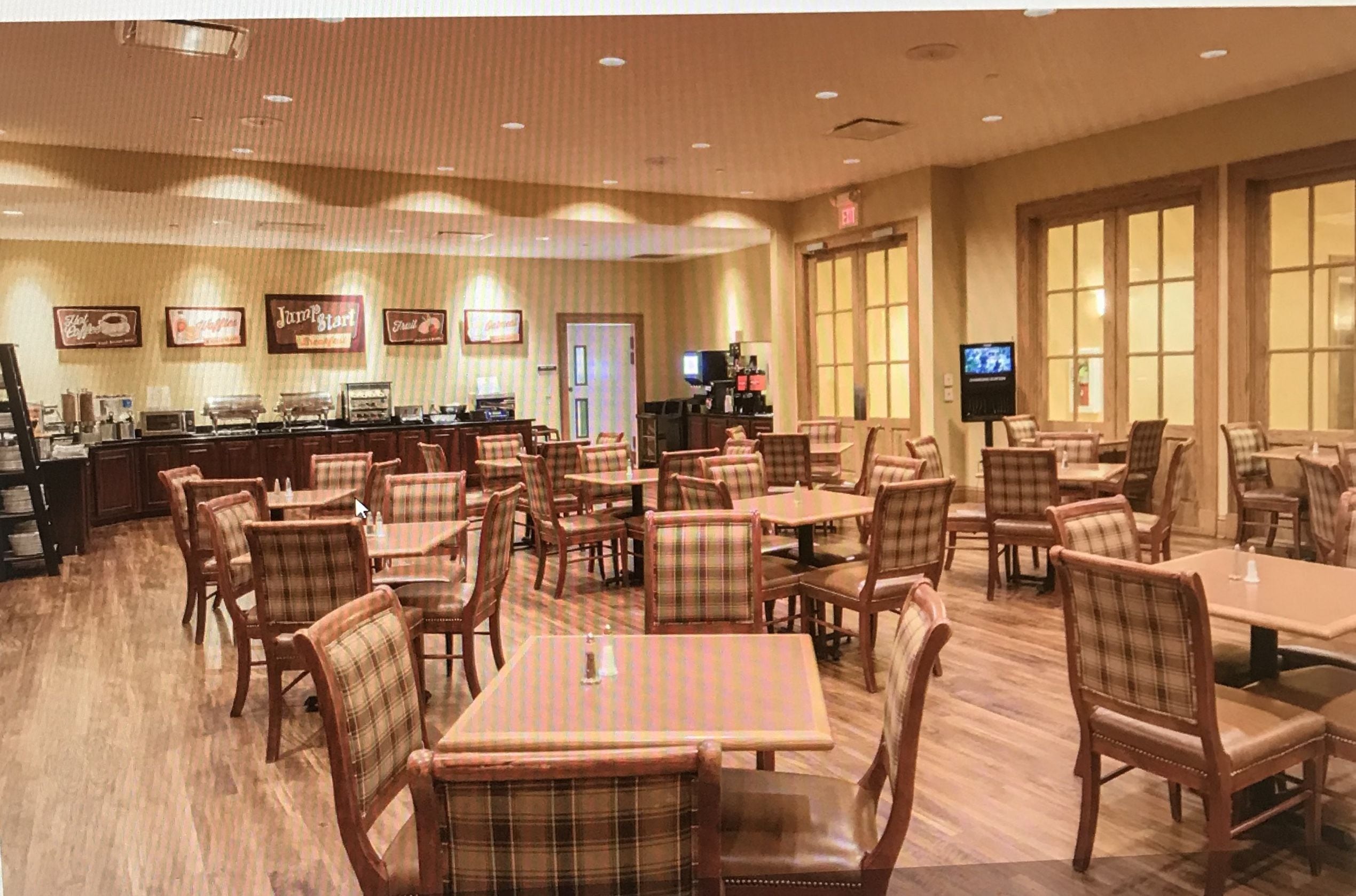 Un restaurant avec plusieurs tables et chaises, un comptoir avec une caisse enregistreuse et un écran de télévision.