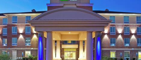 A Holiday Inn Express & Suites hotel with a prominent entrance, columns, and a well-lit facade.