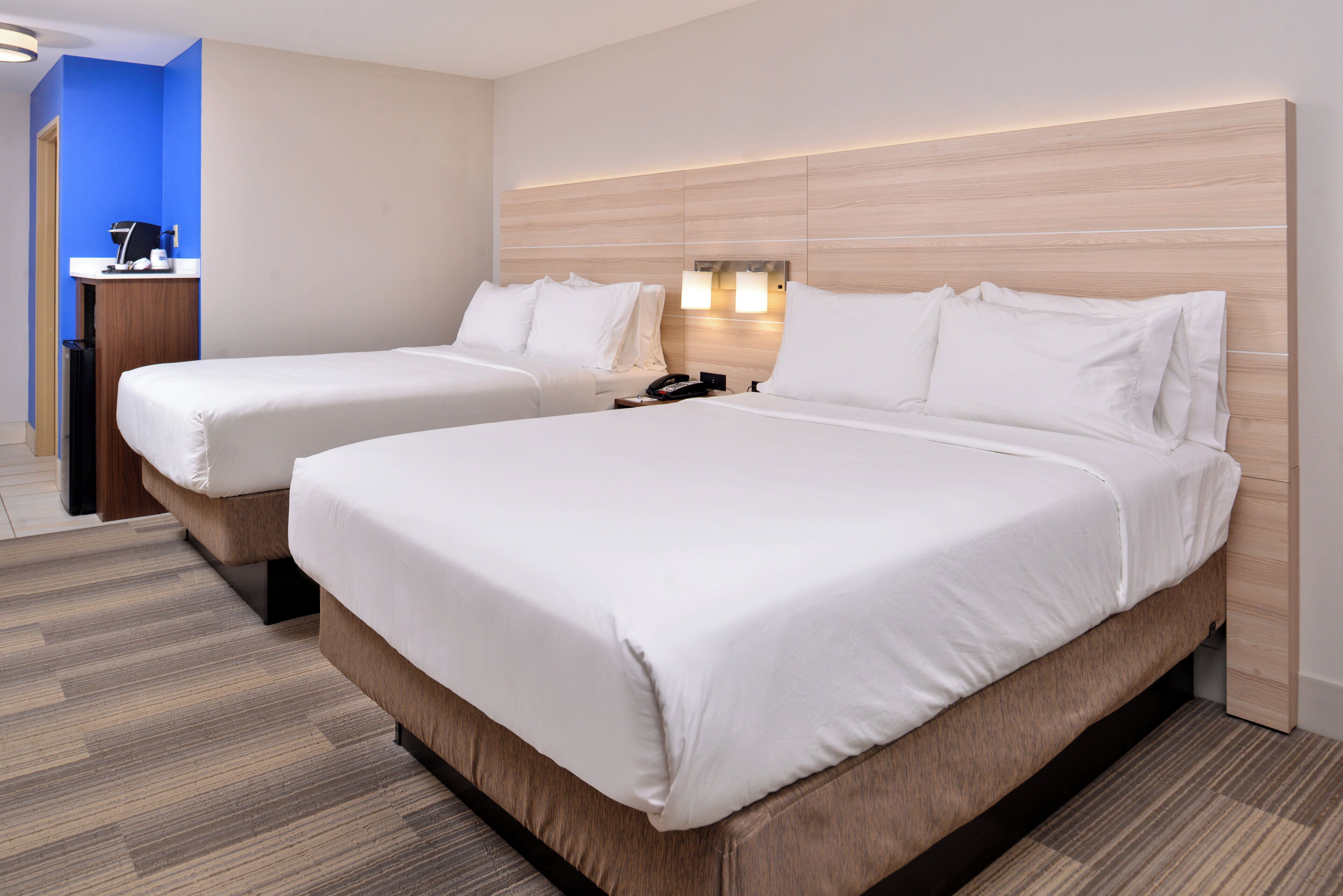 Ein Hotelzimmer mit zwei Betten, einem hölzernen Kopfteil, einem Schreibtisch mit Telefon und einer blauen Wand.