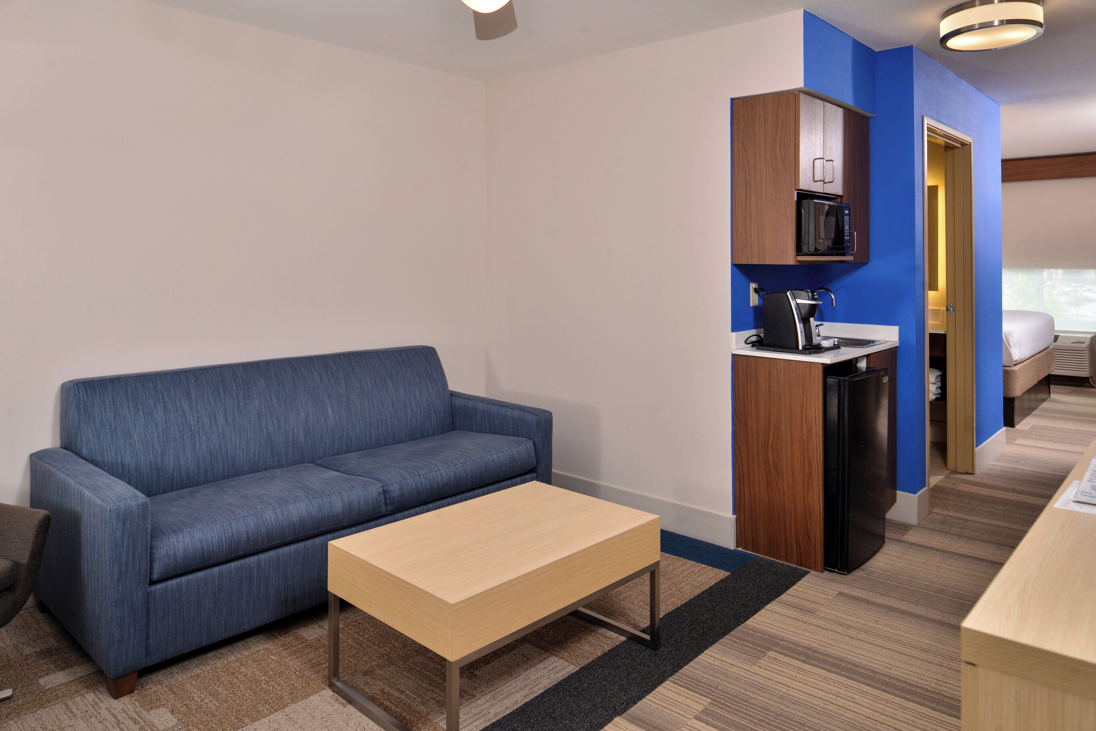 Un espacio habitable compacto con sofá, una mesita, kitchenette con microondas y cama en la habitación contigua.