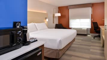 A hotel room with a bed, a desk, a chair, a coffee maker, and a television.