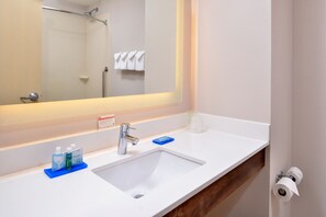 Un baño con lavamanos blanco, un espejo, toallero y zona de ducha.